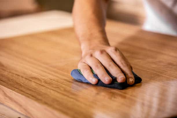 A hand uses a blue cloth to clean or polish a wooden surface.