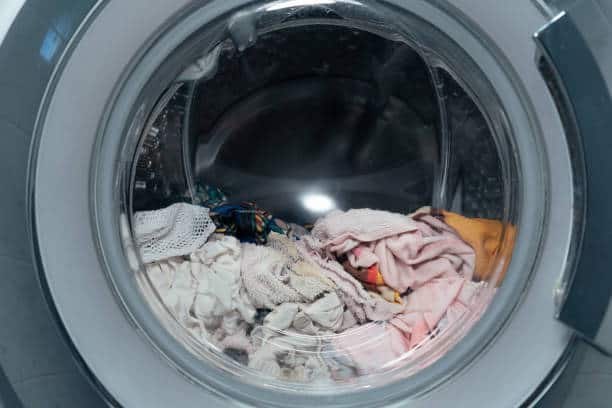 Close-up view of a front-loading washing machine with various clothes inside, ready for washing.