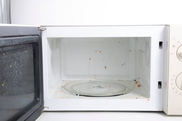 An open microwave oven with food splatters and stains on the interior surfaces.