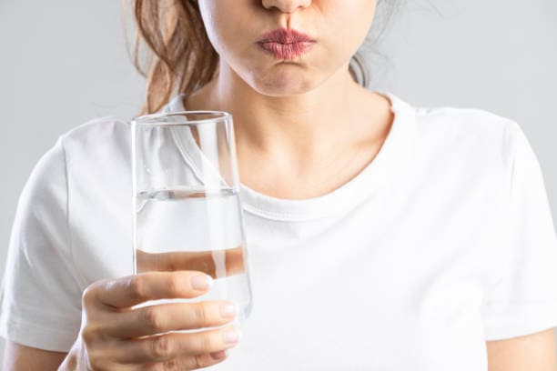 Person holding a glass of water and swishing it in their mouth while wearing a white t-shirt.