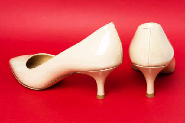 A pair of beige mid-heel shoes on a red background. One shoe is facing forward, the other is turned to the side.