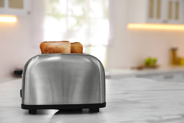 A stainless steel toaster on a kitchen counter with two slices of toasted bread inside.