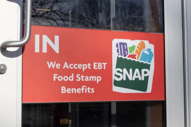 Sign on a glass door reading "We Accept EBT Food Stamp Benefits" with a SNAP logo depicting groceries.