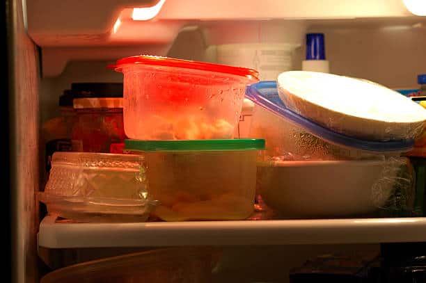 A refrigerator shelf filled with various plastic containers holding food, a bottle on the top right, and other miscellaneous items.