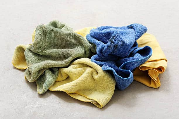 A pile of crumpled cleaning cloths in various colors, including green, yellow, and blue, on a plain surface.