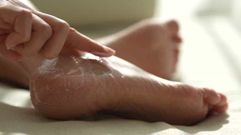 A person applies lotion to the heel of their foot.