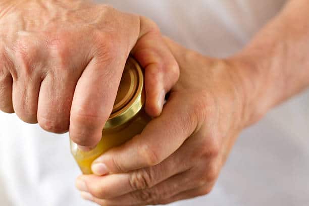 Close-up of hands attempting to open a sealed glass jar with a metal lid.