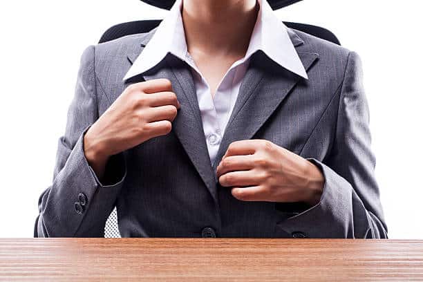Person in a suit sitting at a desk, adjusting the jacket.