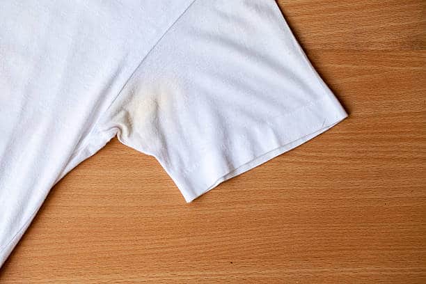 White t-shirt with a visible yellowish stain on the underarm area, placed on a wooden surface.