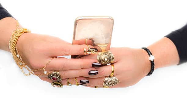 Hands with multiple rings and bracelets holding a smartphone.
