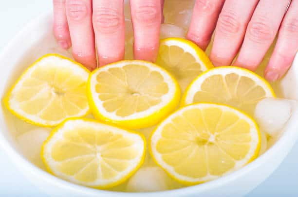 Hands soaking in a bowl with lemon slices, ice, and water.