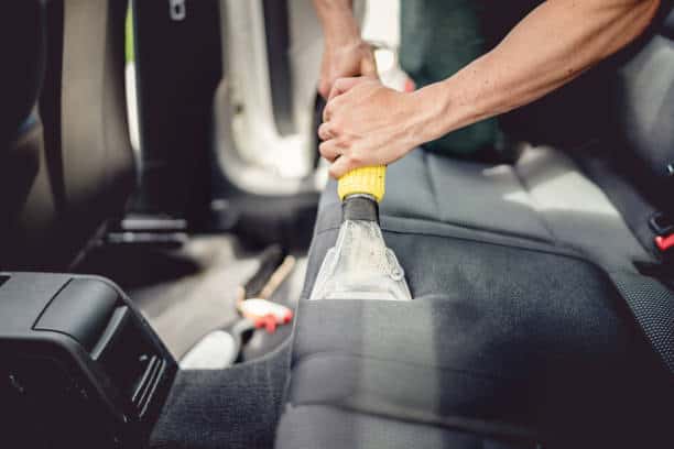 Person cleaning a car seat with a vacuum cleaner in the vehicle's interior.