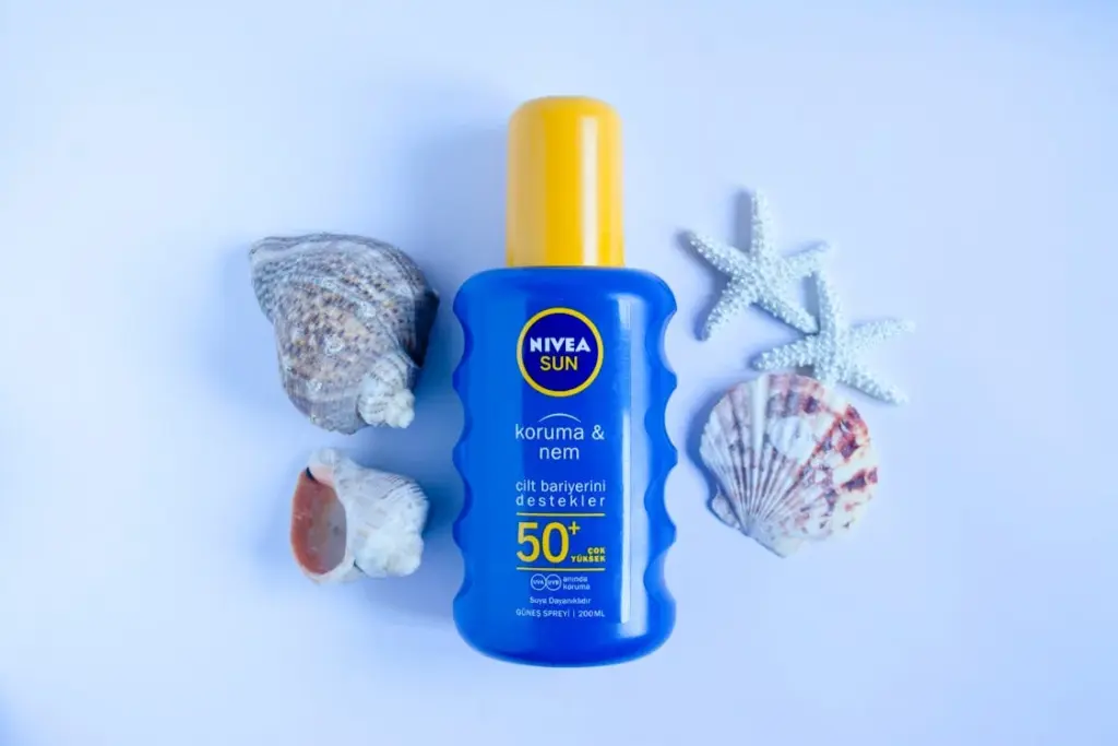 Blue and yellow Nivea Sun SPF 50+ sunscreen bottle surrounded by seashells and starfish on a white background.