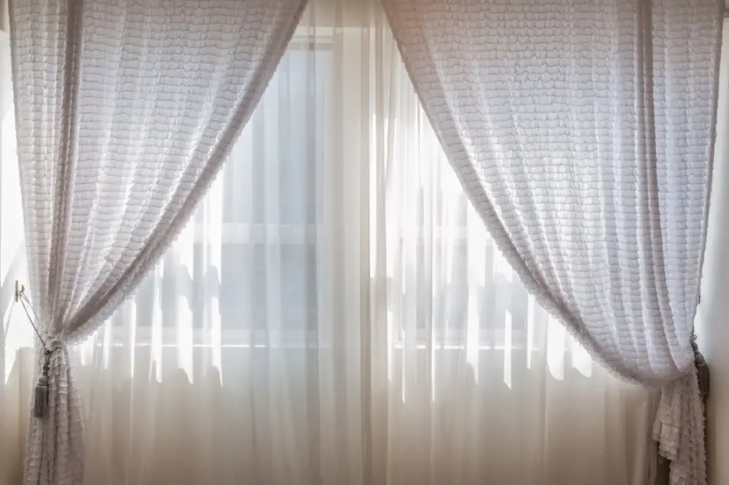 Large window with sheer curtains partially drawn to the sides, letting in soft natural light.
