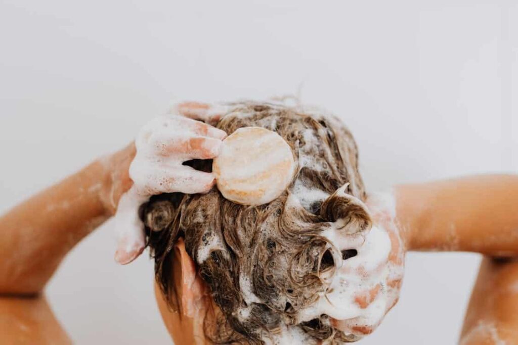 Person washing hair with soap and lather, hands massaging the scalp.