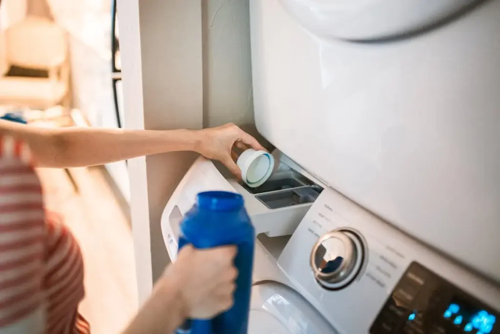 Person pouring liquid detergent into a washing machine drawer.