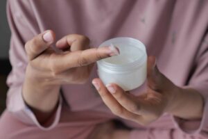 Person scooping cream from a white container with their finger.