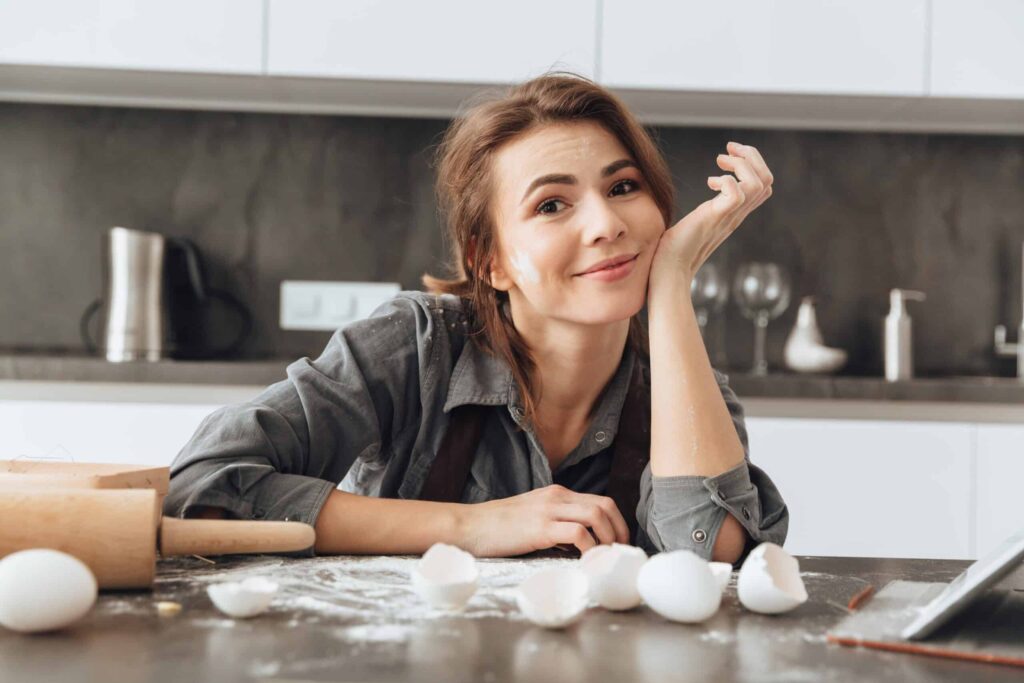 Person in a kitchen smiling, surrounded by eggshells and baking items.