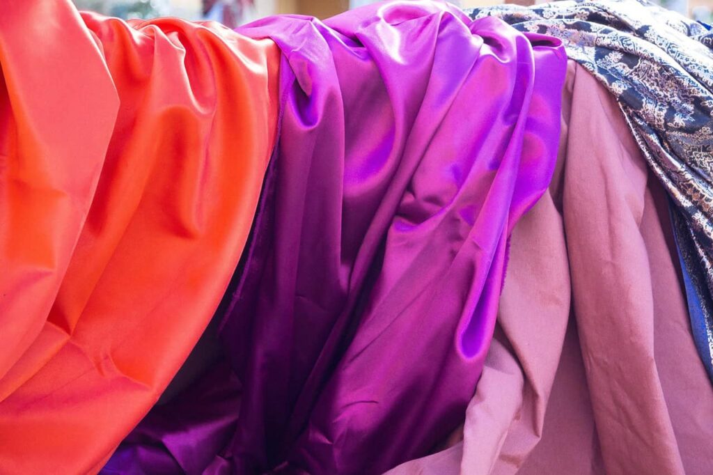 Colorful fabric draped in folds, featuring shades of orange, purple, pink, and patterned blue.