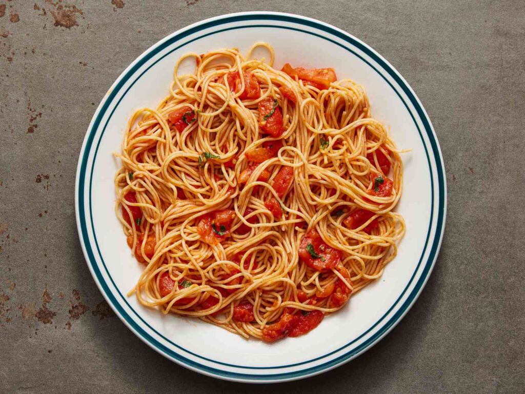 A plate of spaghetti with tomato sauce is served on a gray surface.