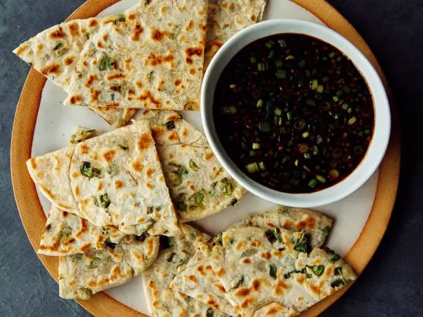 Plate of sliced scallion pancakes with a bowl of dark dipping sauce.