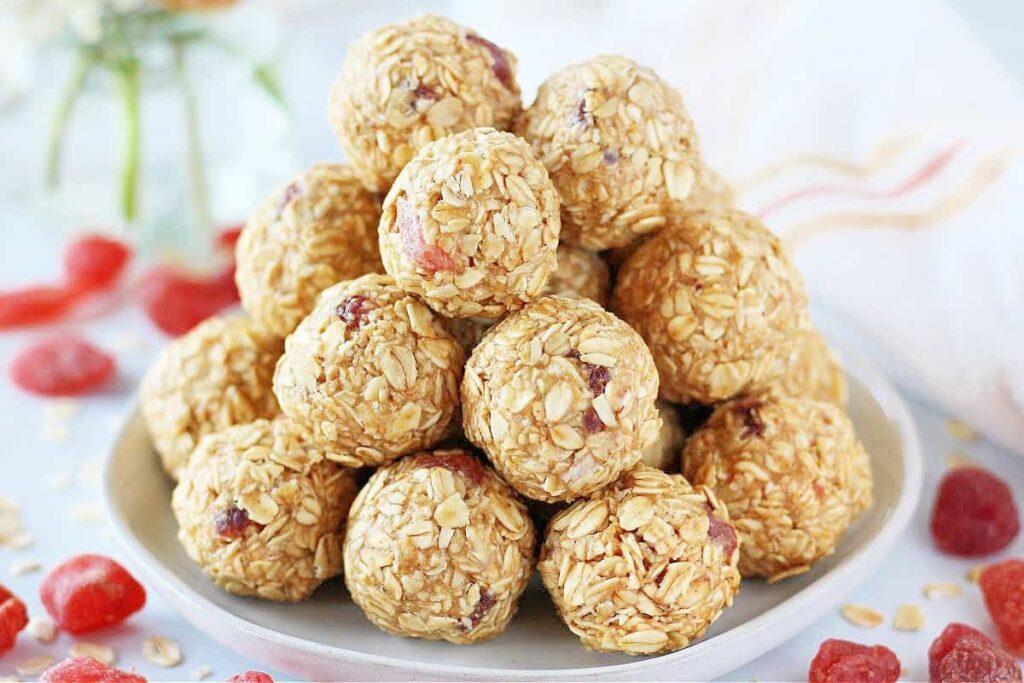 A plate of stacked oatmeal energy balls with visible bits of dried fruit, surrounded by scattered dried fruit pieces.
