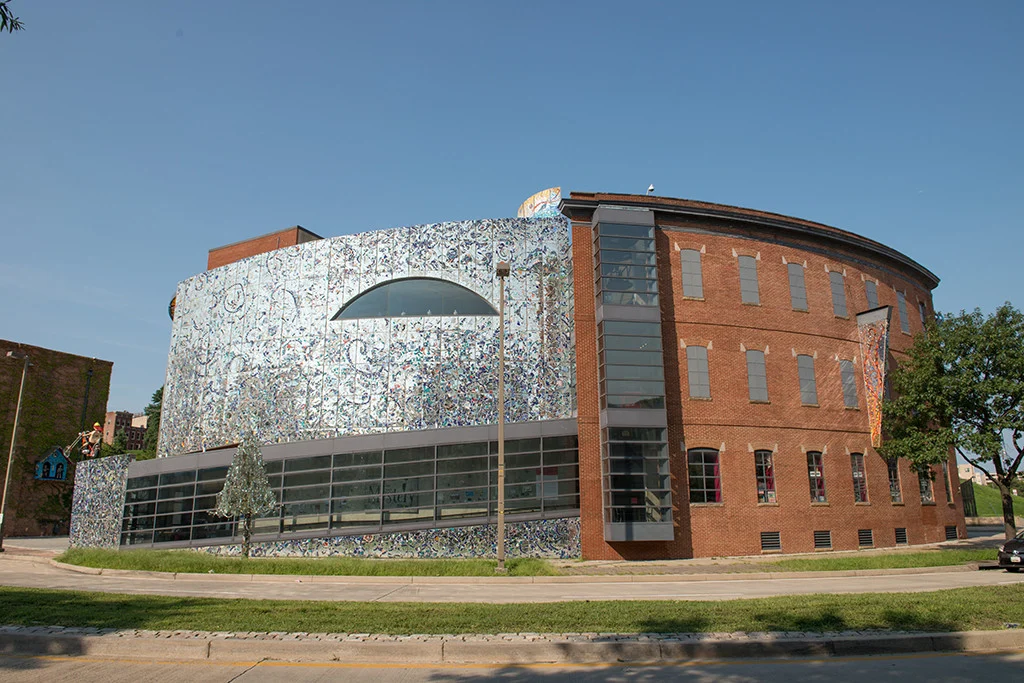 A modern brick and metallic mosaic building with large windows, featuring a unique circular section and artistic exterior design.