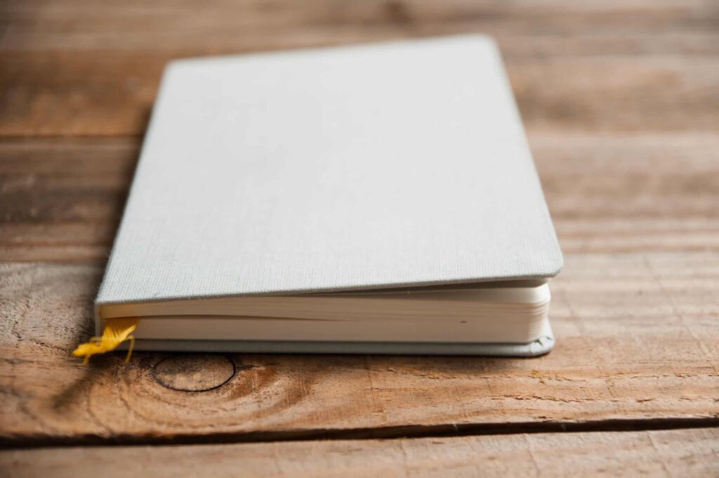 A closed gray notebook with a yellow ribbon lies on a wooden surface.