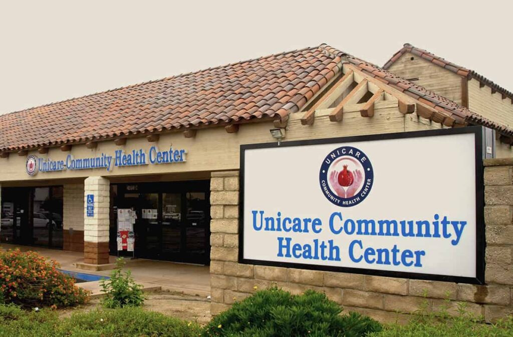 Exterior of Unicare Community Health Center with a large sign in front and a tiled roof.