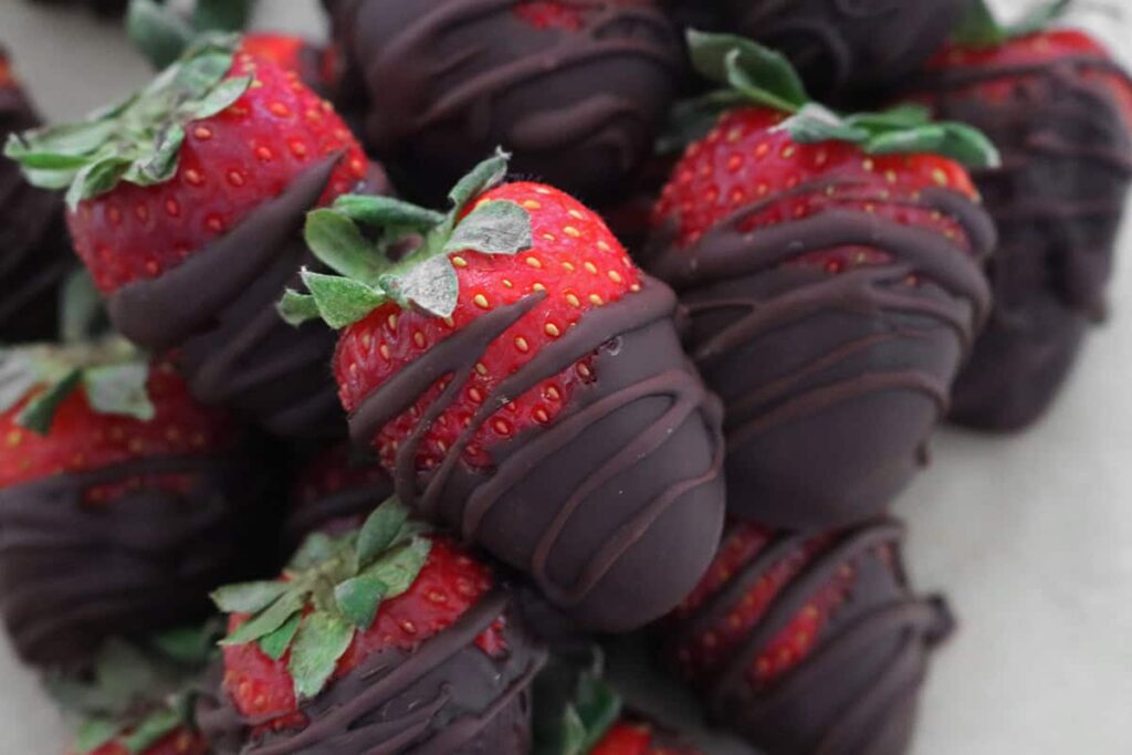 Close-up of strawberries dipped in dark chocolate, arranged in a pile.