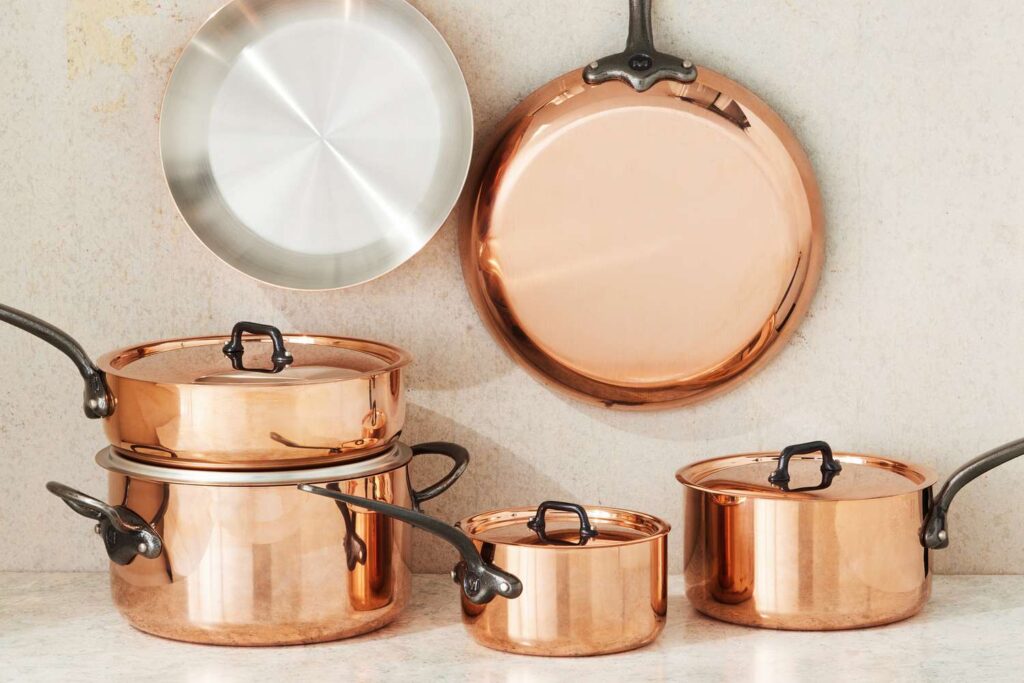 A set of copper pots and pans with black handles, displayed neatly against a beige wall.