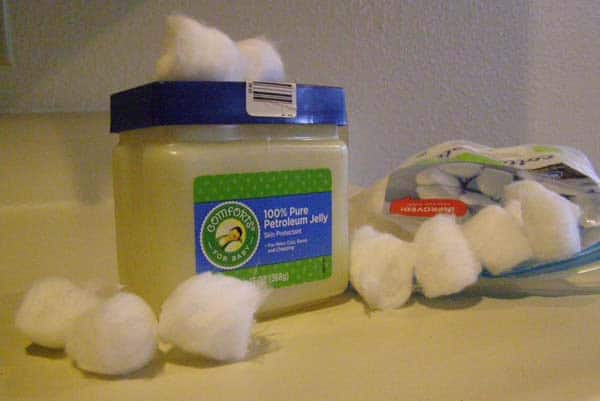 A jar of petroleum jelly with cotton balls scattered around it on a surface.