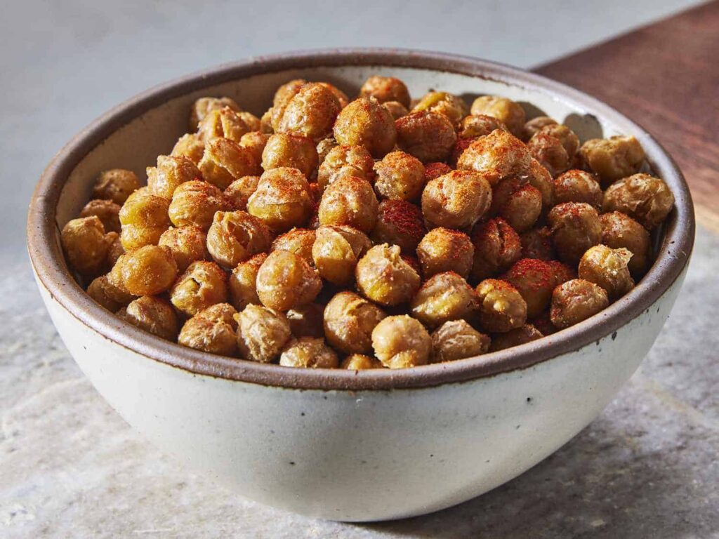 A bowl of roasted chickpeas seasoned with spices on a stone surface.