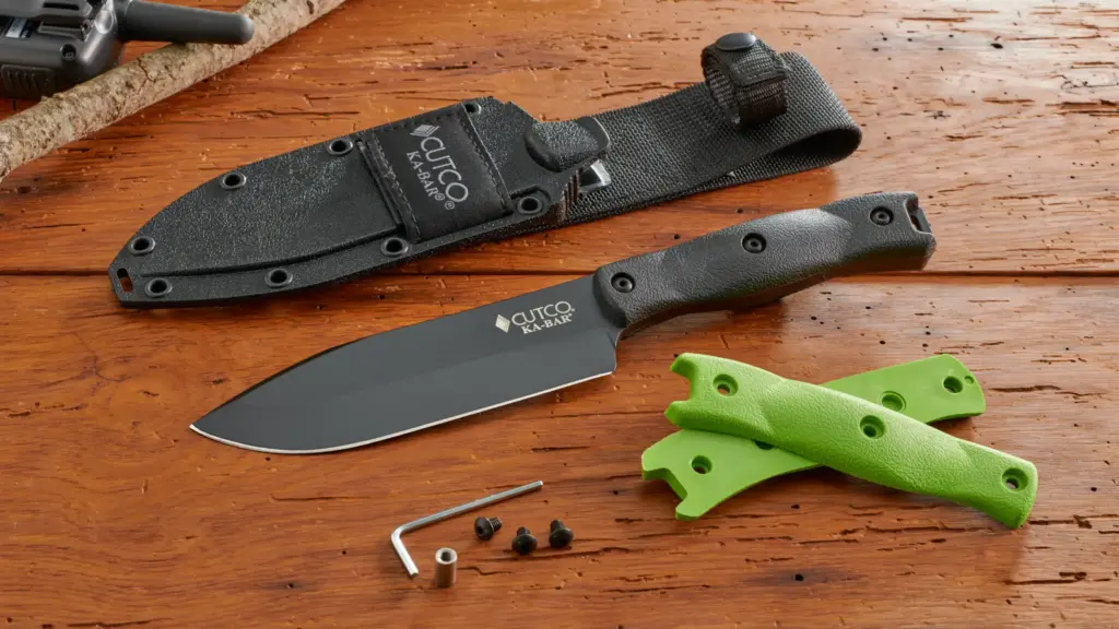 Knife with black blade and handle, green interchangeable grips, screws, hex key, and sheath on a wooden surface.