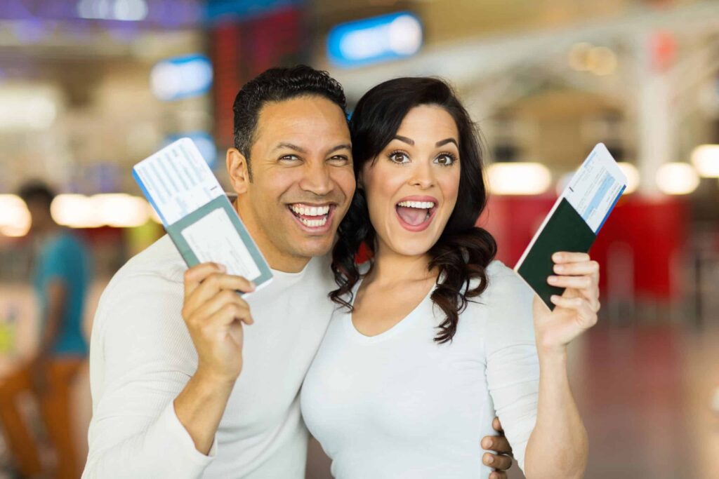 A smiling couple holds up passports with boarding passes in an airport.