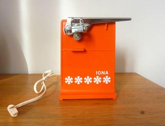 Orange vintage IONA electric can opener with floral design on a wooden table.