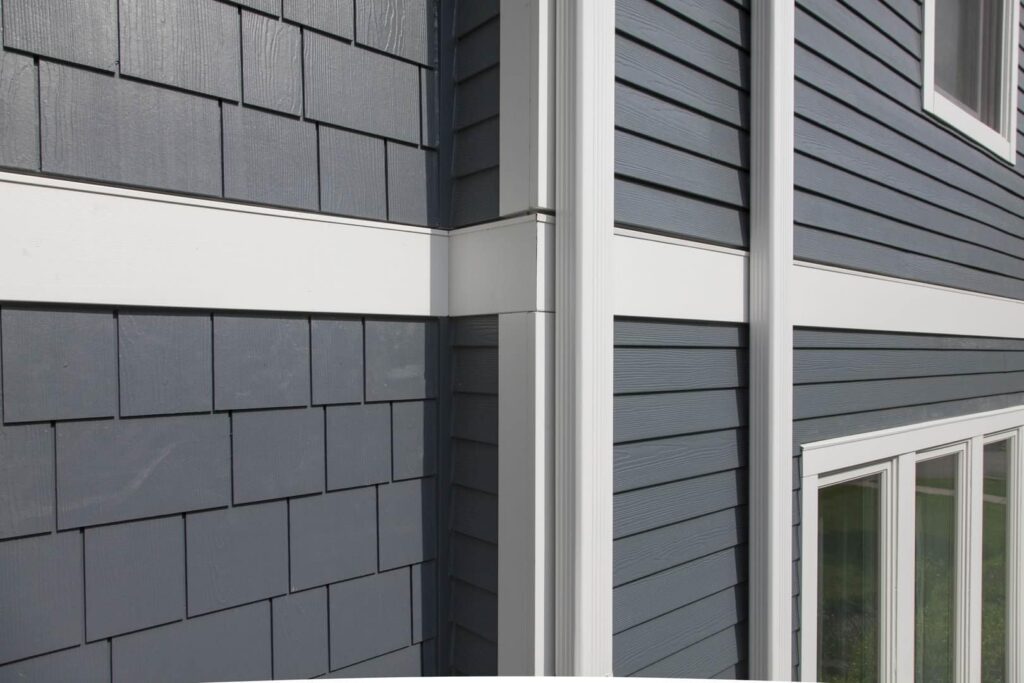 Close-up view of a modern building exterior with blue-gray horizontal and shingle siding, featuring white trim and two vertical windows.