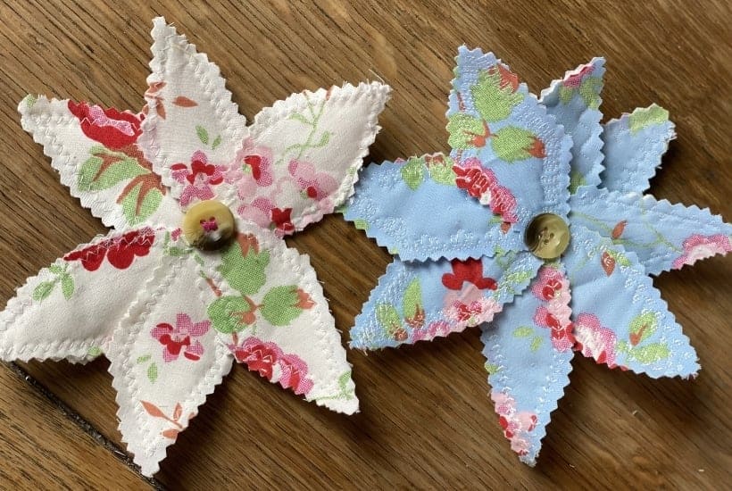 Two fabric star-shaped flowers with floral patterns and button centers on a wooden surface.