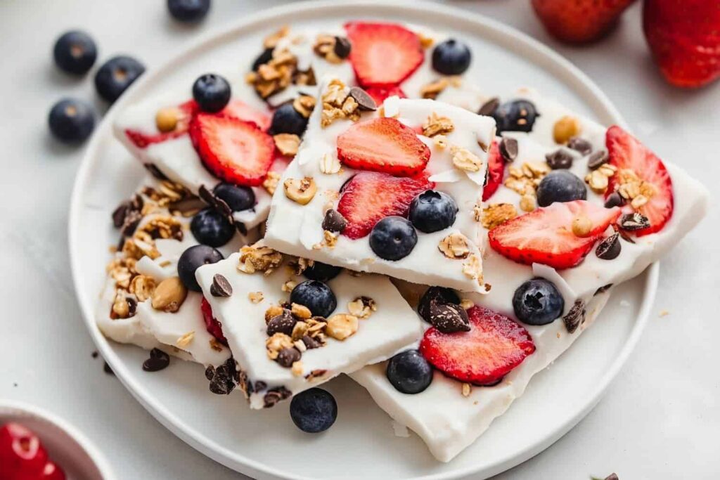 A plate of yogurt bark topped with sliced strawberries, blueberries, granola, and chocolate chips.