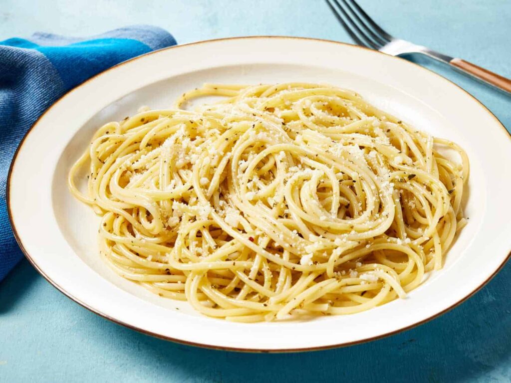 A plate of spaghetti with grated cheese on top. A blue napkin and a fork are placed beside the plate.