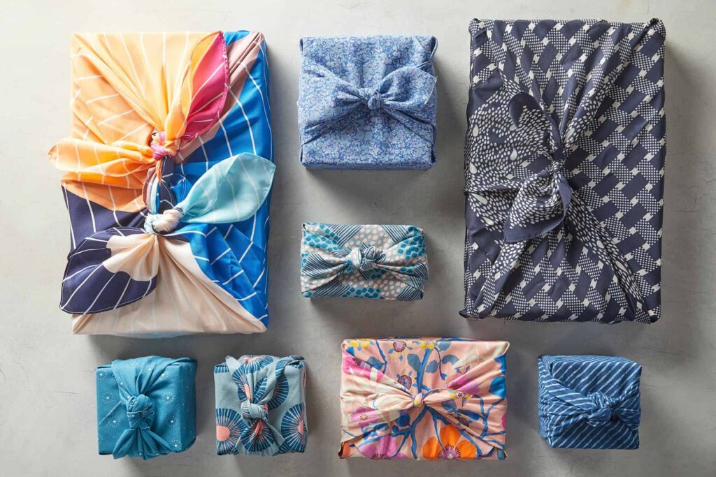Colorful gifts wrapped in patterned fabric, each tied with a bow, arranged neatly on a light surface.
