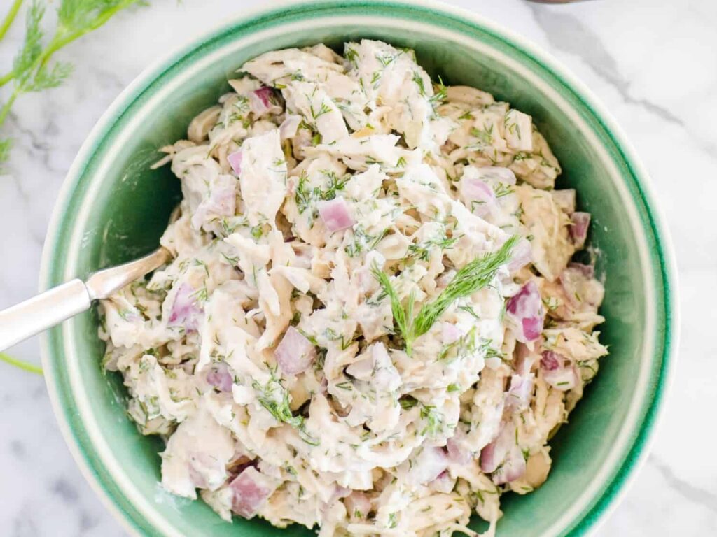 A green bowl filled with a creamy salad, featuring diced red onions, shredded chicken, and fresh dill.