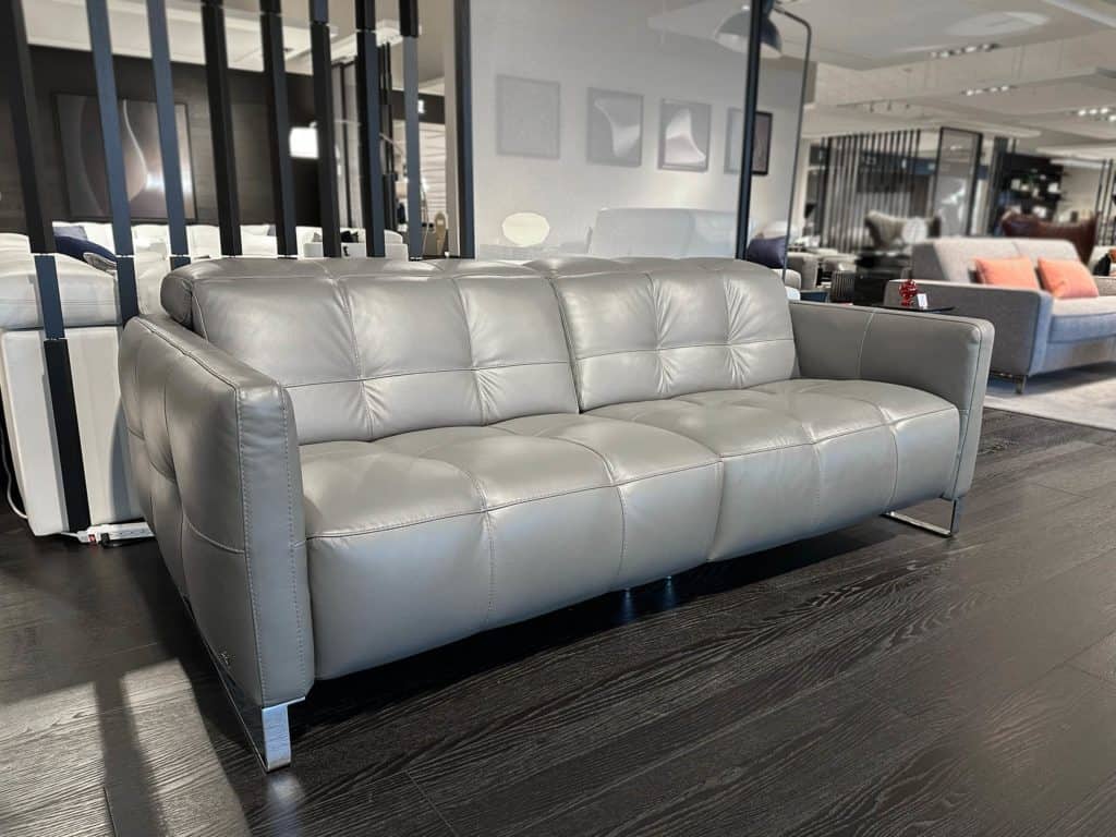 Gray leather sofa with tufted cushions in a modern showroom setting.