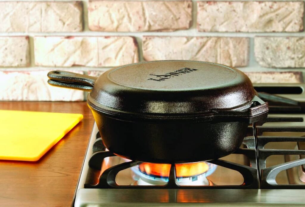 A cast iron skillet with a lid on a gas stove, with a yellow cutting board nearby.