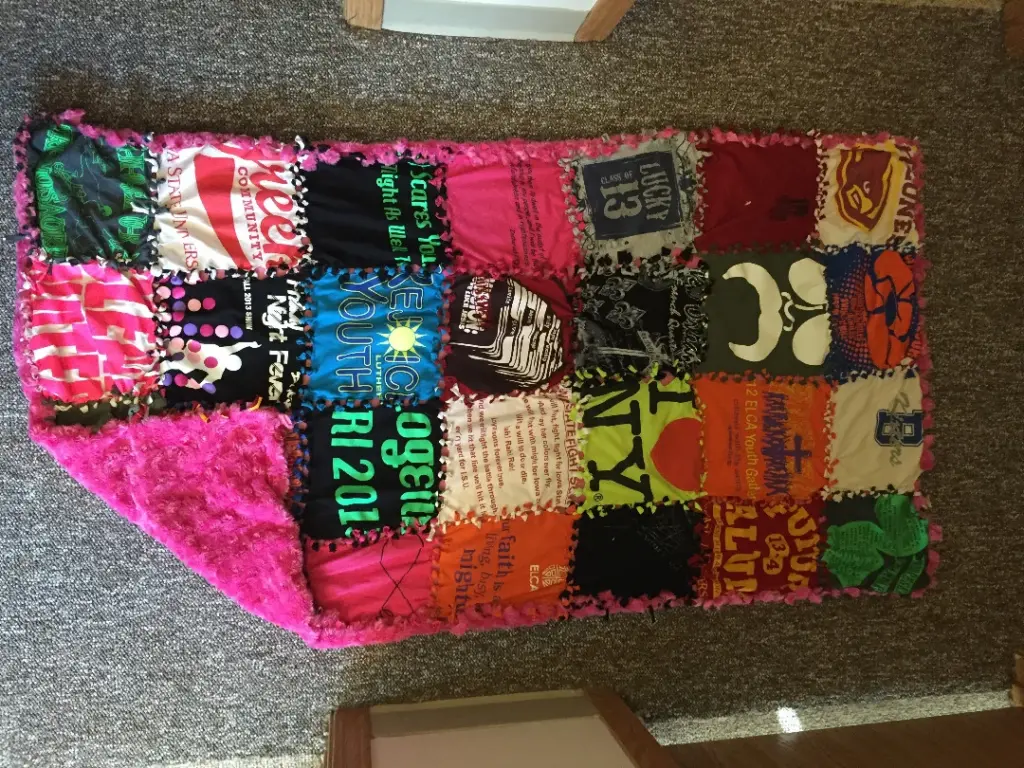 A colorful quilt made from various t-shirts, featuring logos and text in different fonts and colors, lies on a carpeted floor.