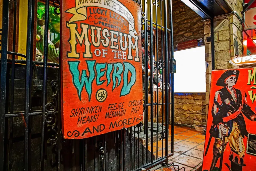 Sign for "Museum of the Weird" advertising exhibits like shrunken heads, Fiji mermaid, and cyclops pig, with colorful pirate artwork nearby.