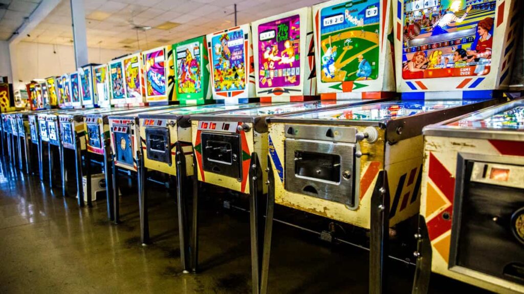 A row of vintage pinball machines in a brightly lit arcade.