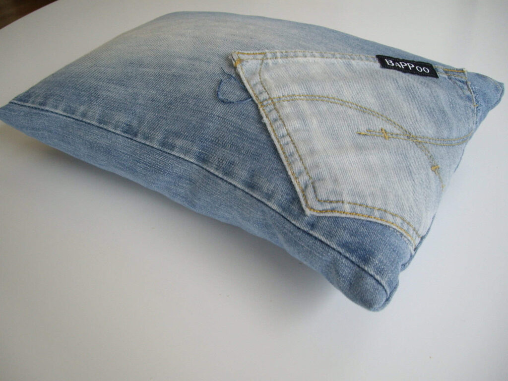 A pillow covered in denim fabric with a pocket and a black label.