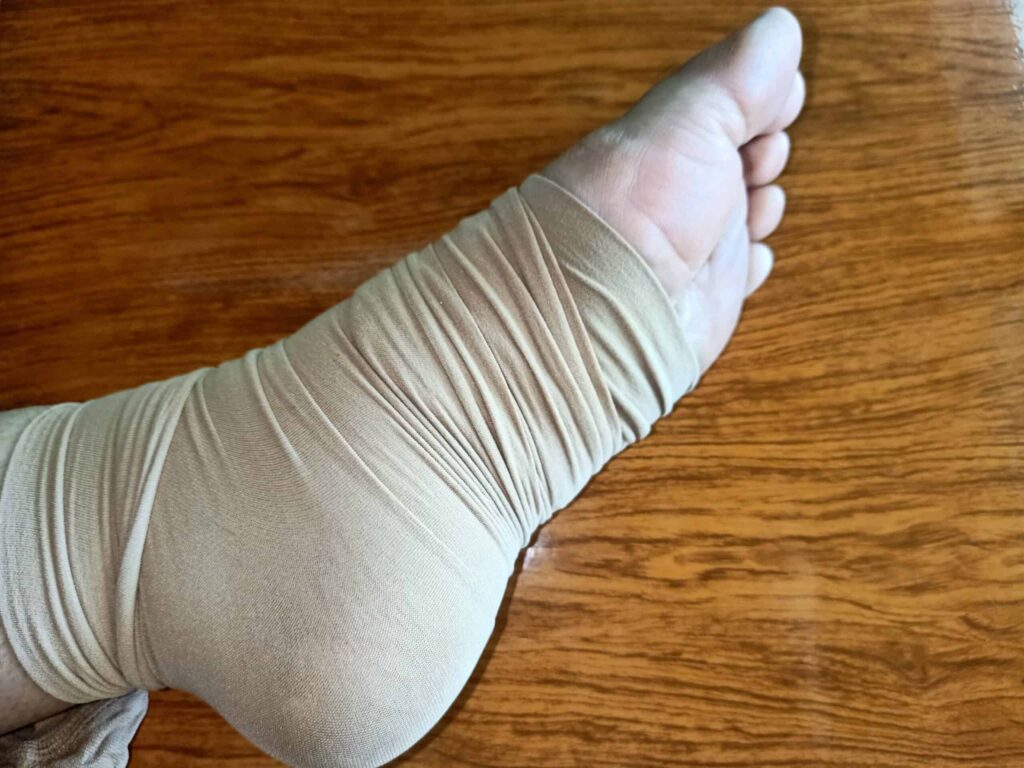 A foot wrapped in a beige compression bandage rests on a wooden surface.