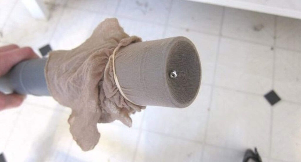 A vacuum cleaner hose with pantyhose secured by a rubber band at the opening, used on a tiled floor.